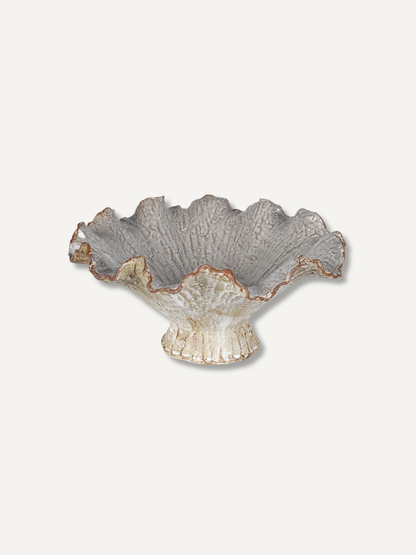 A ruffled ceramic bowl with a textured, leaf-like pattern in gray and cream, featuring a subtle copper-brown glaze along the rim, set against a solid off-white background.