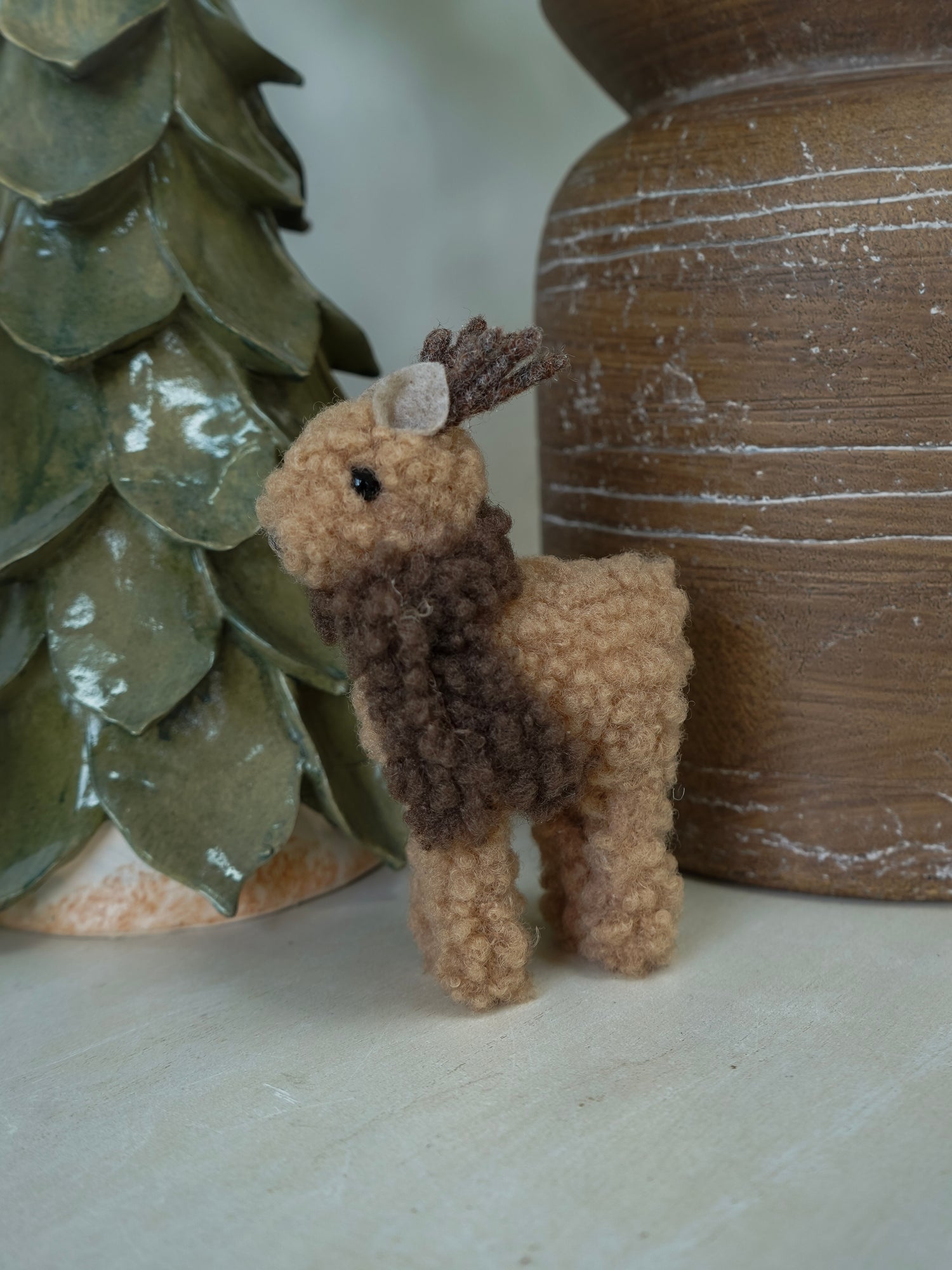 Small brown deer figurine next to a textured green vase and wooden object.