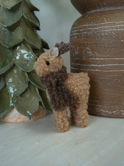 Small brown deer figurine next to a textured green vase and wooden object.