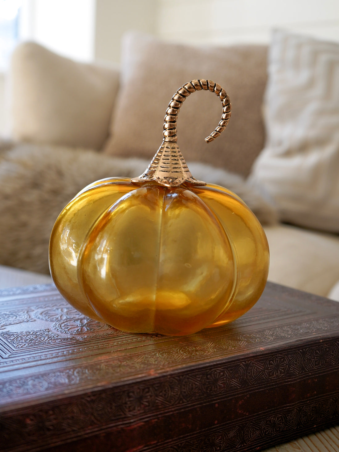 Decorative glass pumpkin with a gold stem on a wooden table.
