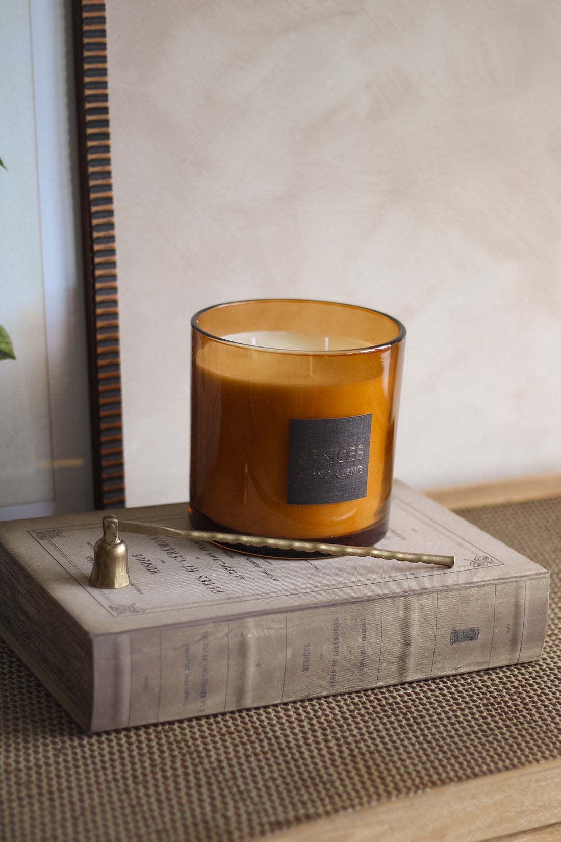 Amber glass candle with a label on a book, with a small brass candle snuffer beside it.