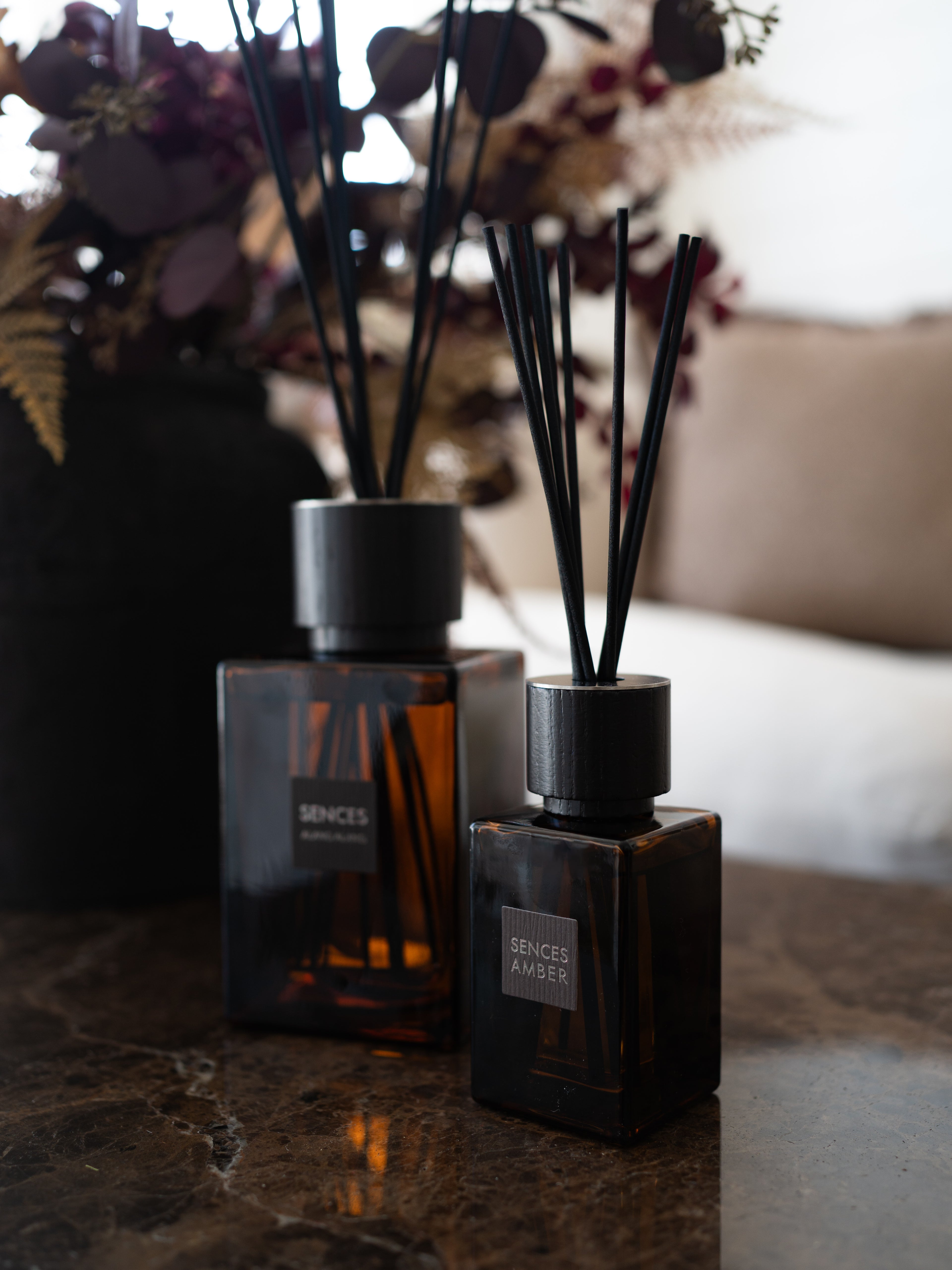 Two amber glass reed diffusers with black caps and black reeds, labeled &