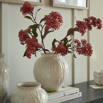 Decorative arrangement with red flowers in a white vase on a shelf.