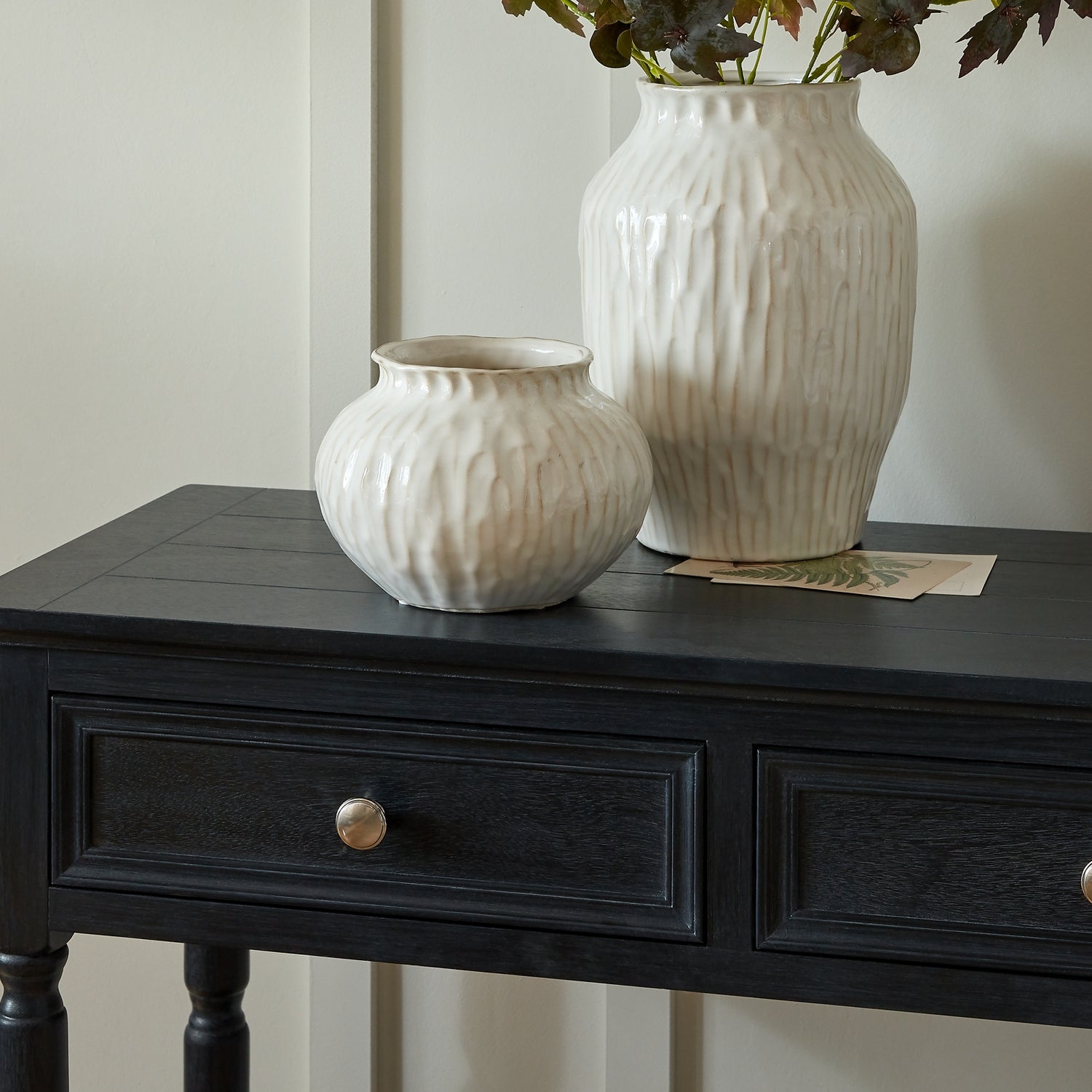 Two white textured vases on a black wooden table with a neutral background