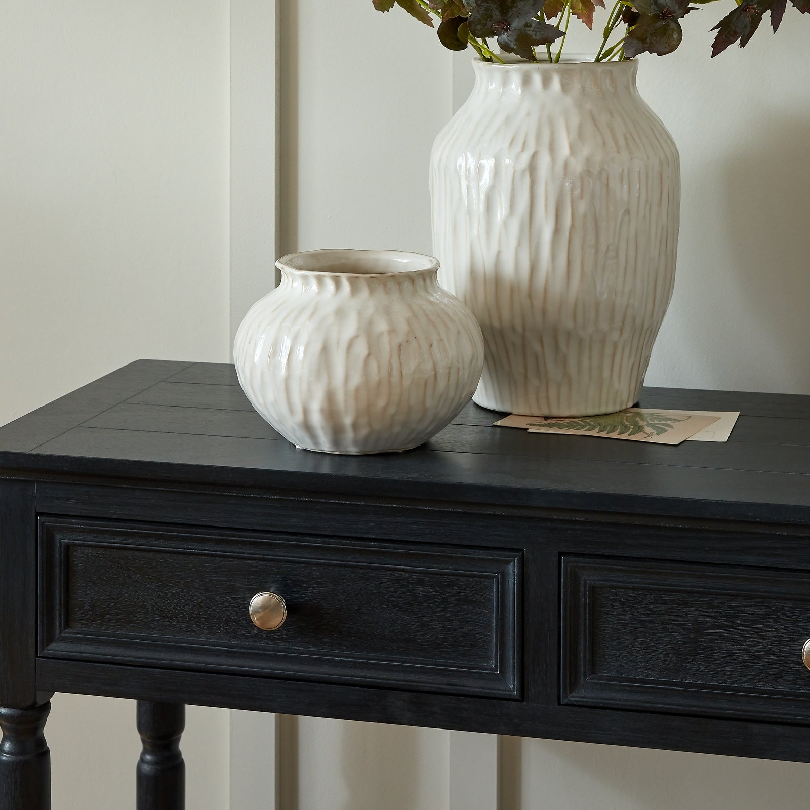 Two white textured vases on a black wooden table with a neutral background