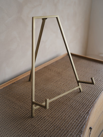 Antique brass easel stand on a textured surface with a neutral background