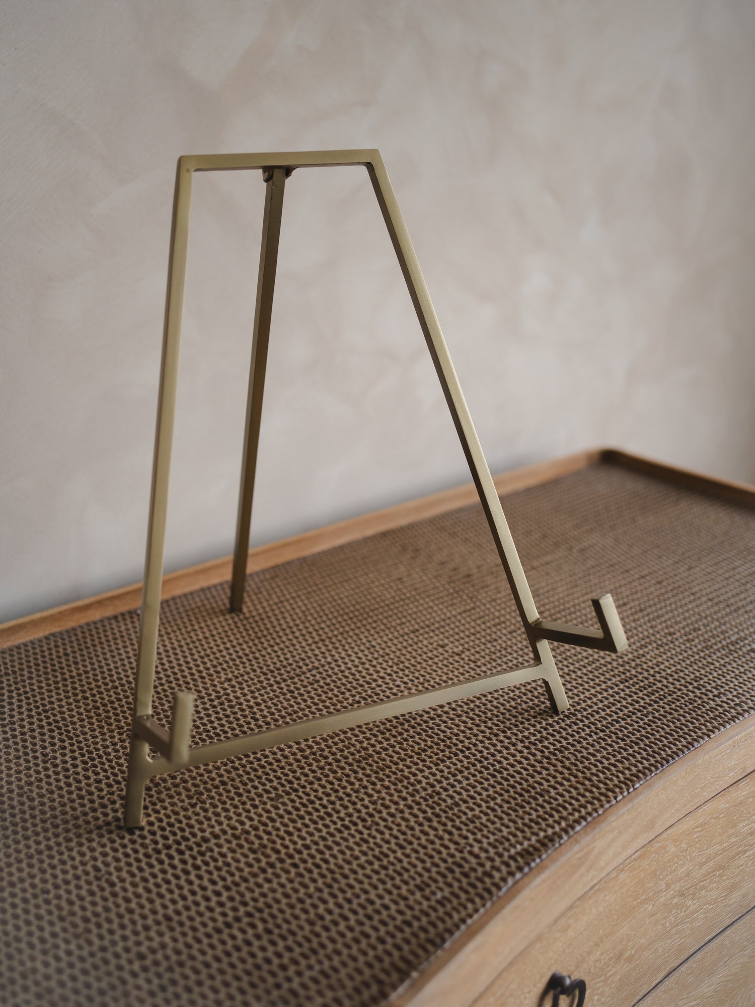 Gold metal antique brass easel stand  on a textured surface with a neutral background