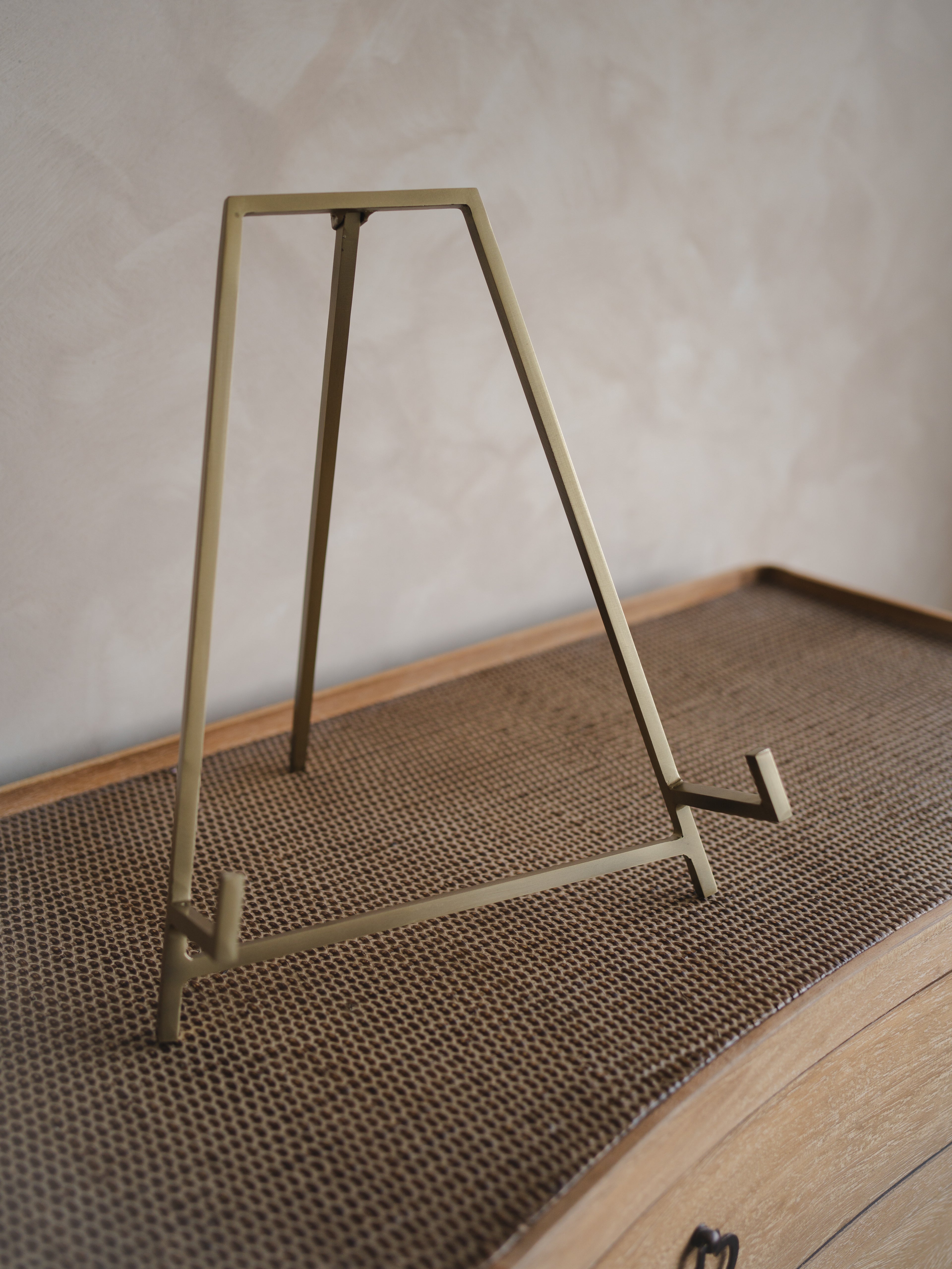 Gold metal antique brass easel stand  on a textured surface with a neutral background