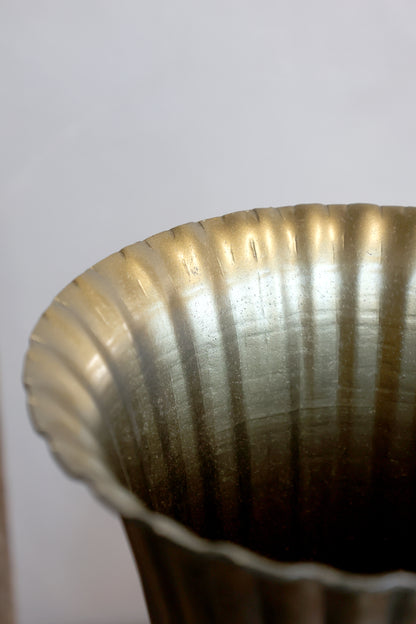 Close-up of a metallic fluted cup or vase rim with a brushed gold and silver finish against a plain light background.