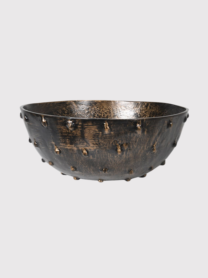 Decorative bowl with textured surface and small studs on a light gray background