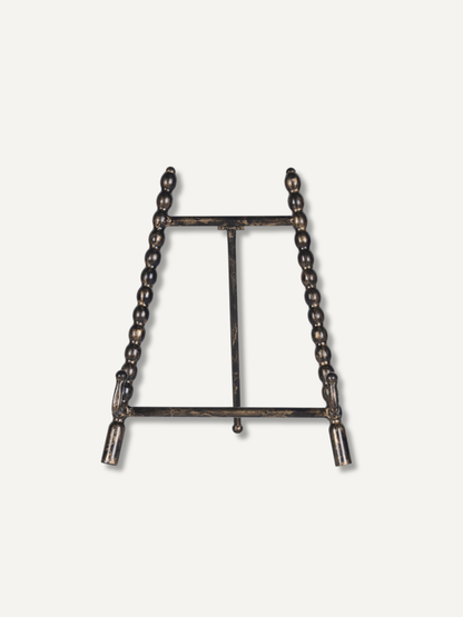 A dark metal tabletop easel stand with beaded vertical side supports and a central support bar, shown against a plain off-white background.