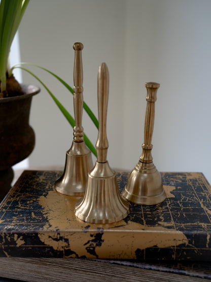 Three brass bells on a textured surface with a plant in the background