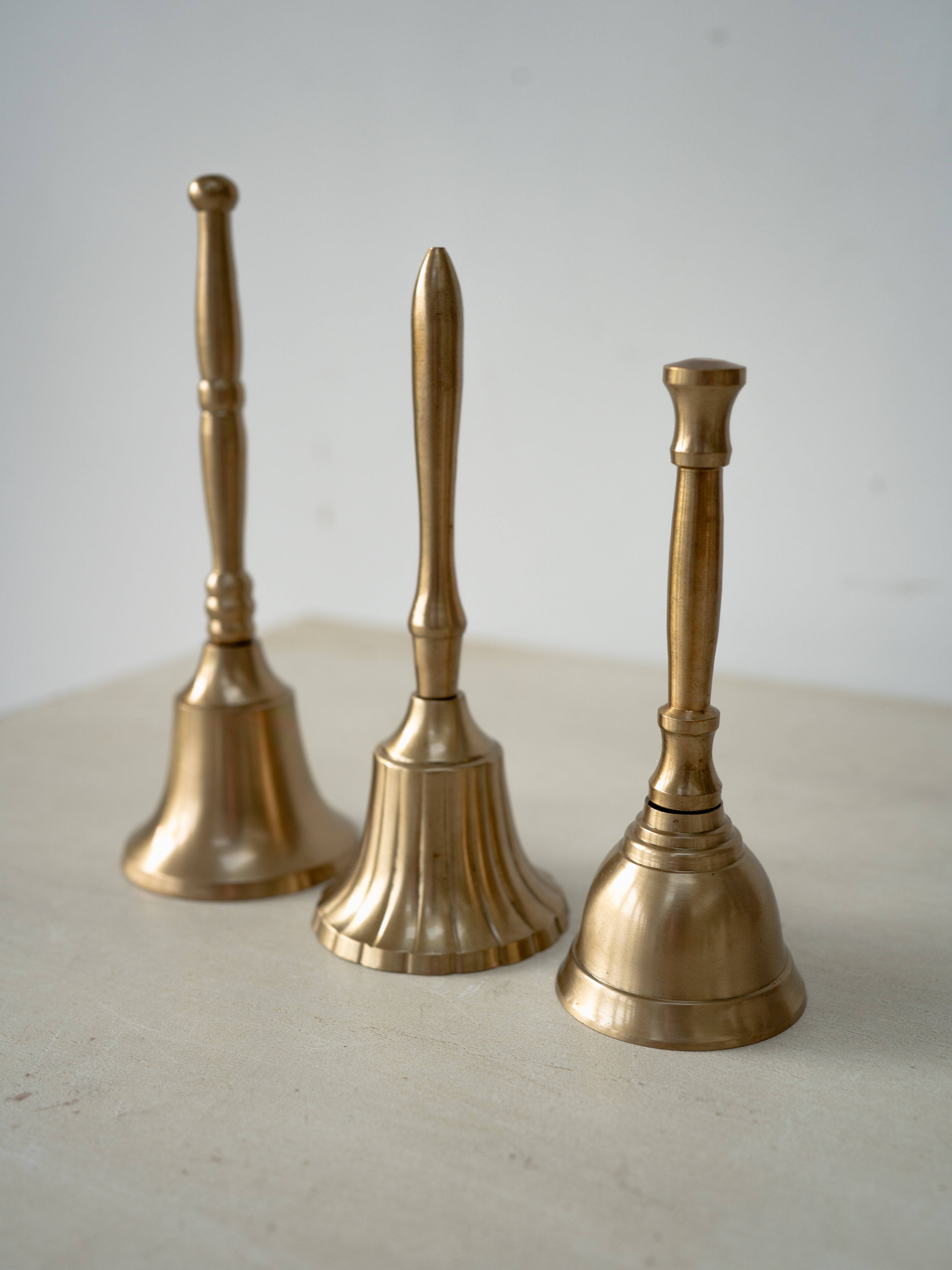 Three brass hand bells of different sizes on a light surface with a white background