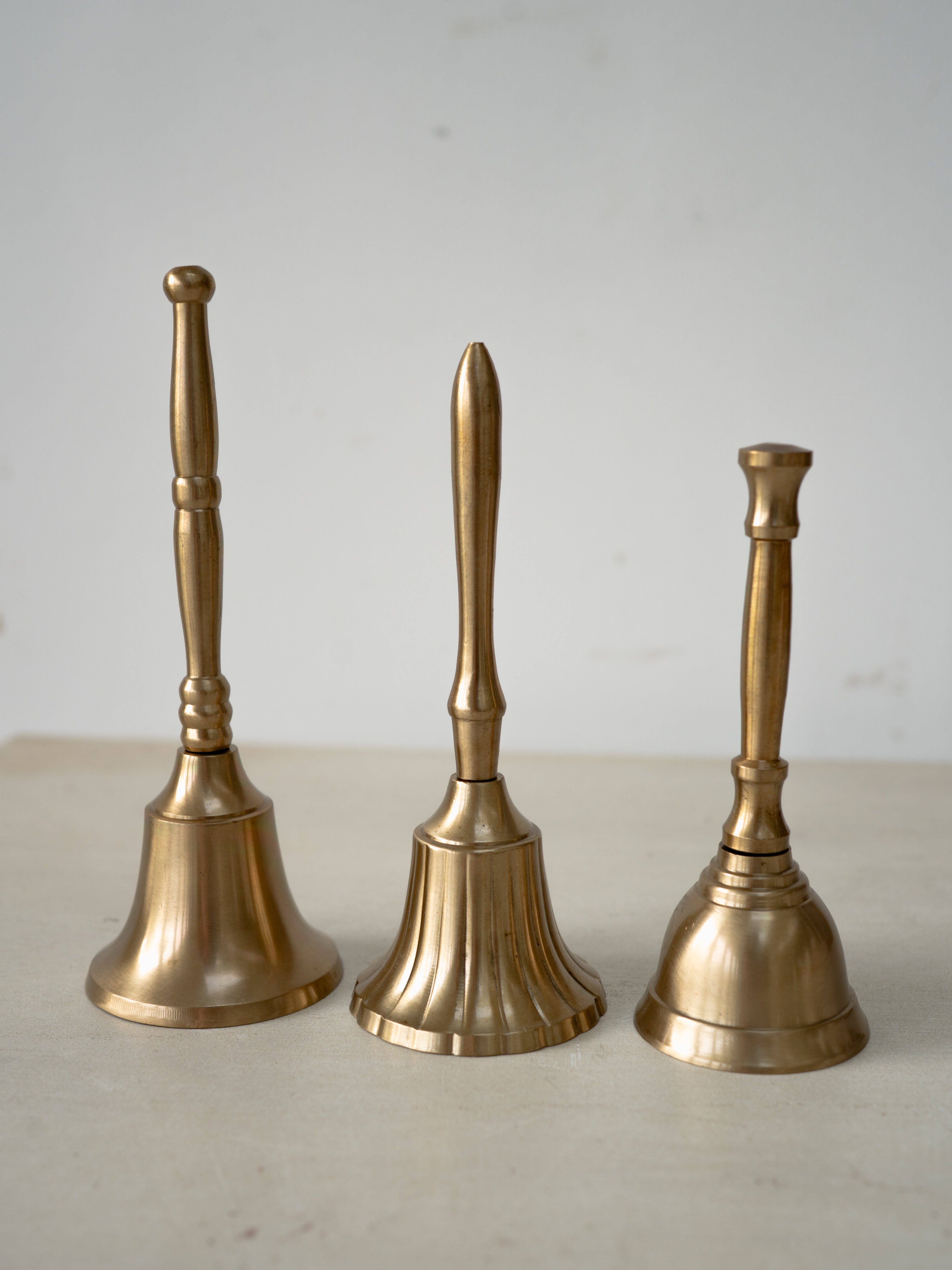Three brass bells of different sizes on a light surface with a neutral background