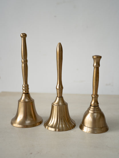 Three brass bells of different sizes on a light surface with a neutral background