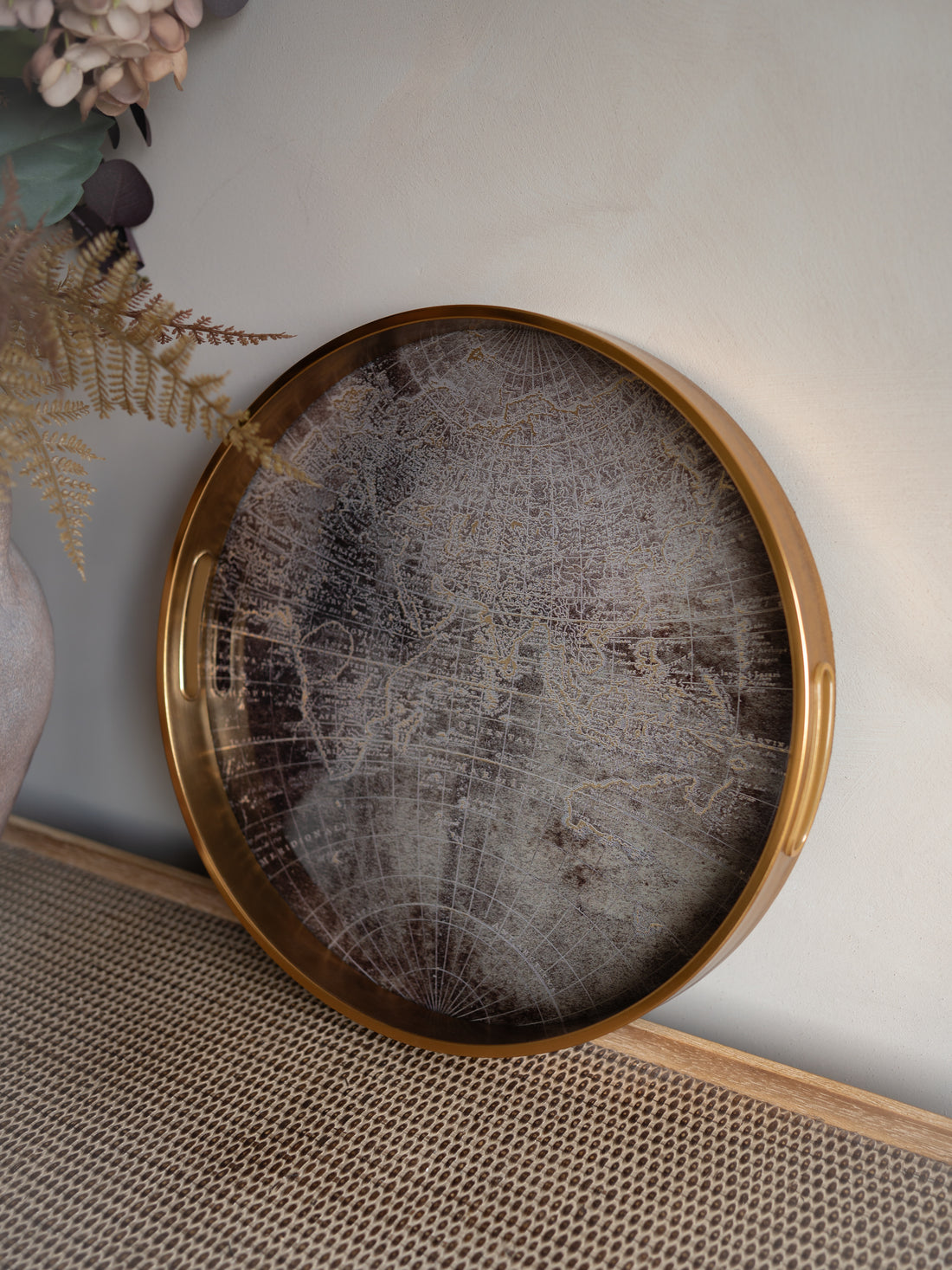 Antique Gold World Map Round Tray on its side with faux flowers in the background