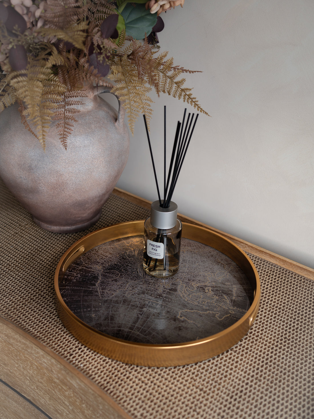 Diffuser bottle with reeds on a decorative tray next to a vase and plants.