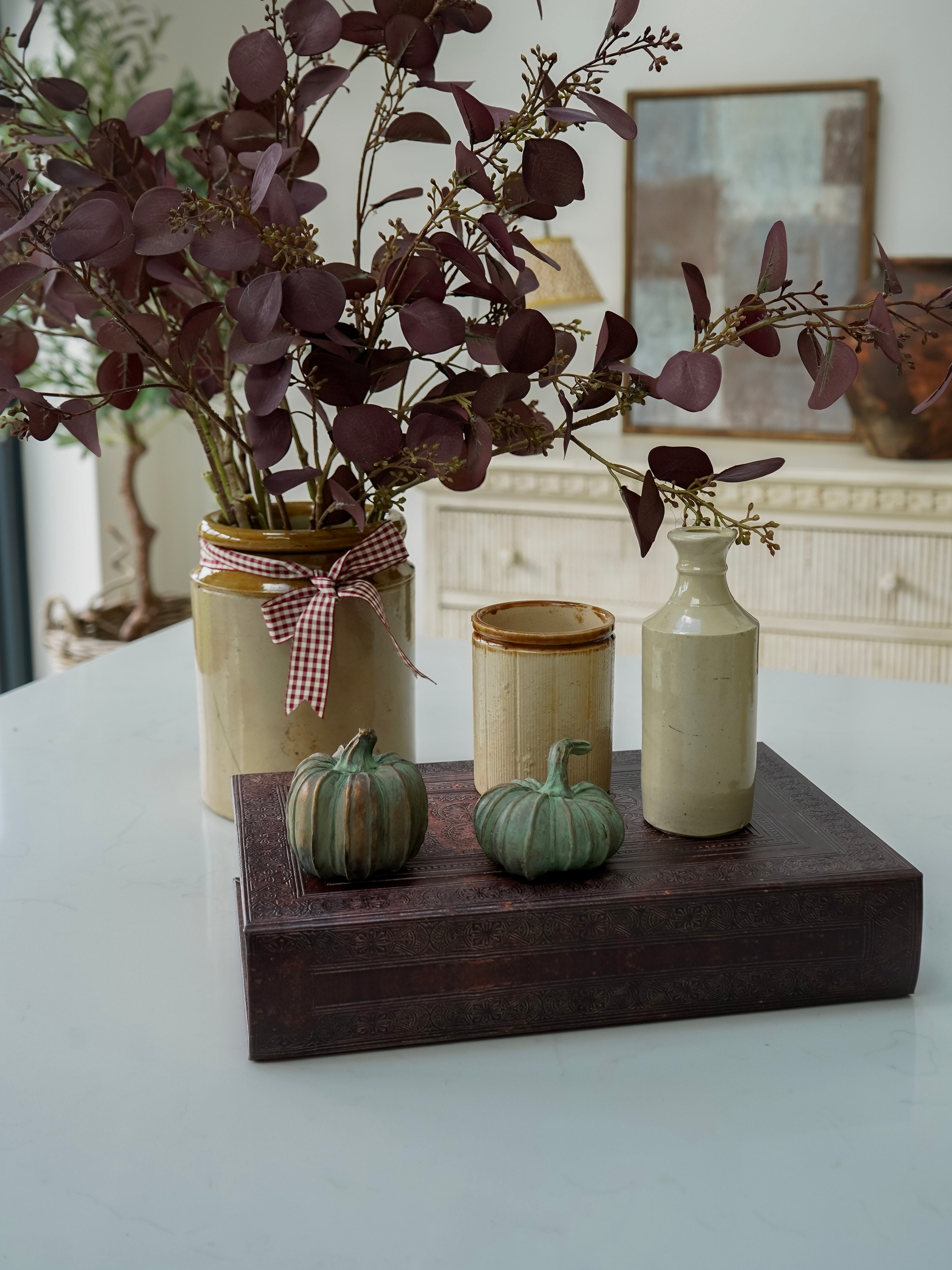 Decorative arrangement with jars, pumpkins, and a plant on a wooden block.