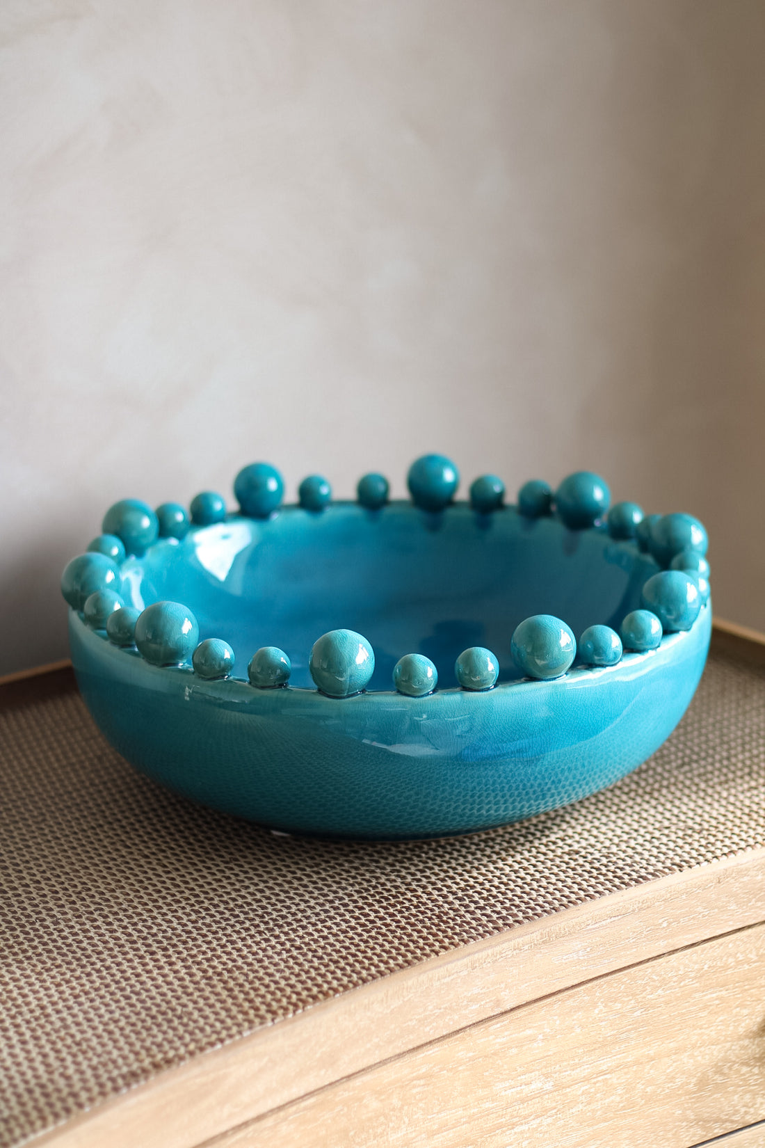 Aqua ceramic bowl with bobble-like embellishments on a neutral background