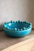 Aqua ceramic bowl with bobble-like embellishments on a neutral background