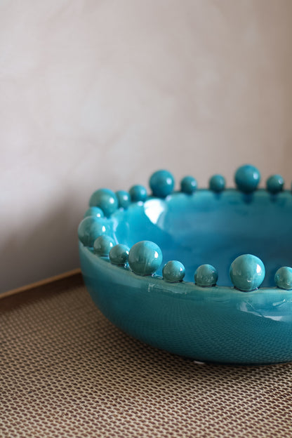 aqua bowl with bobble edge detailing on a textured surface
