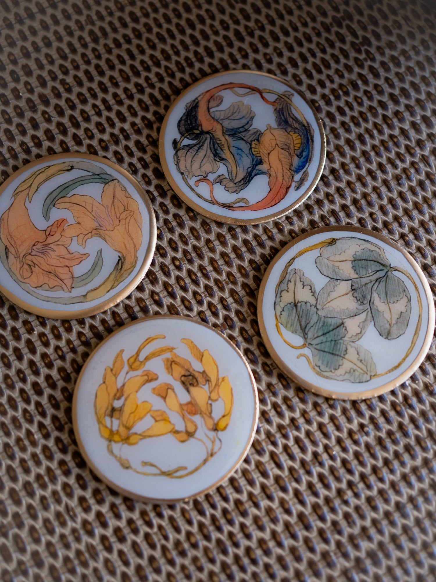 Four round metal coasters with floral designs on a textured surface.