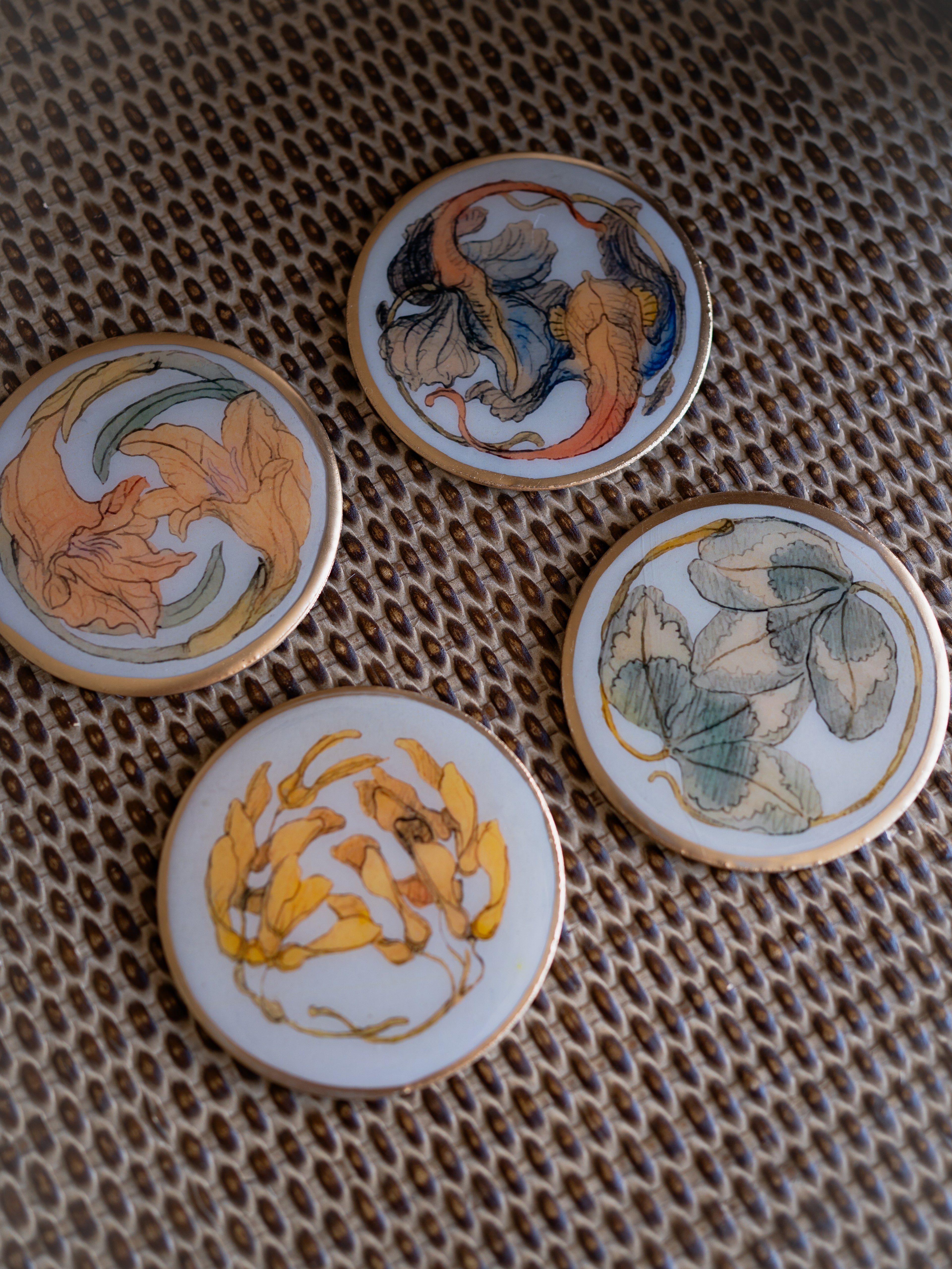 Four round metal coasters with floral designs on a textured surface.