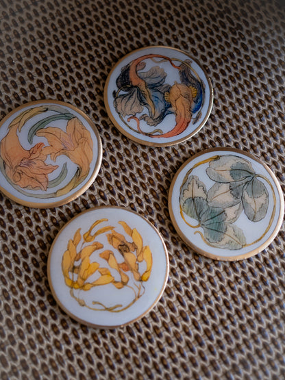 Four round metal coasters with floral designs on a textured surface.