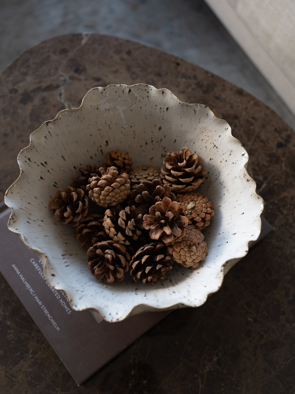 rustic pine cones in cream speckled bowl on brown marble coffee table