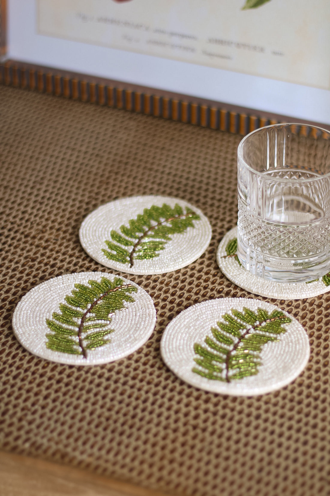 Set of four coasters with leaf design on a textured surface with a glass of water.