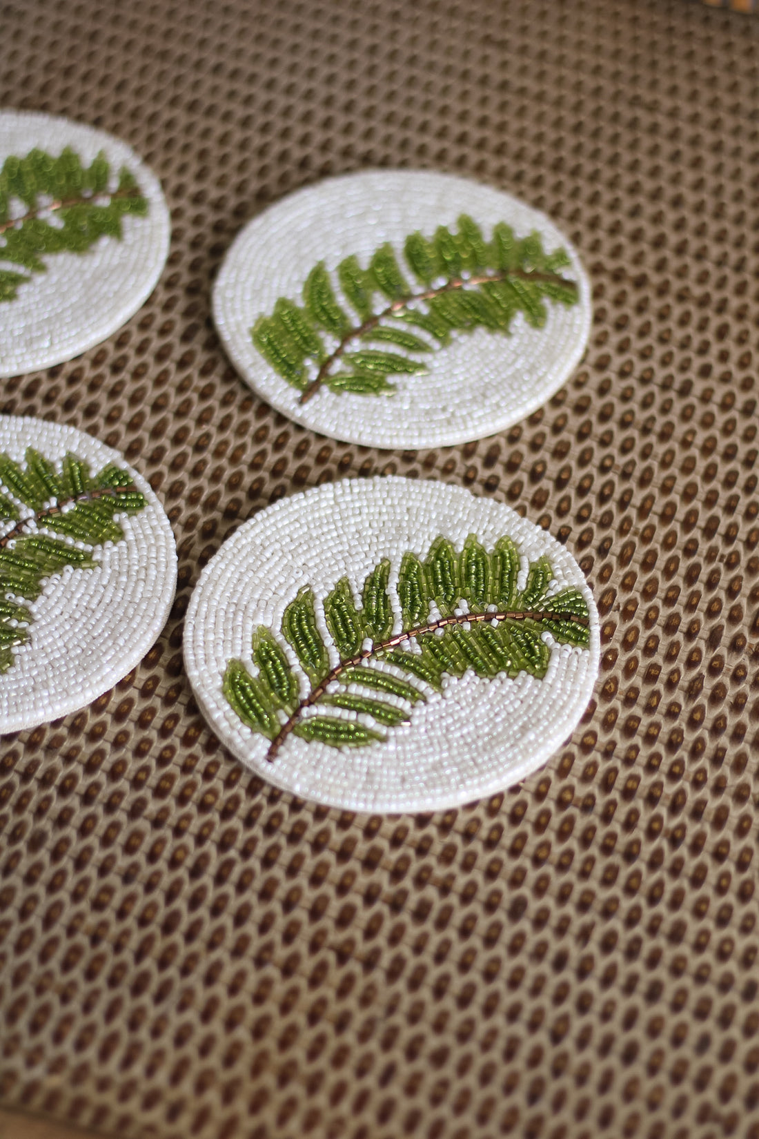 Set of four round embroidered coasters with green leaf patterns on a textured brown surface.