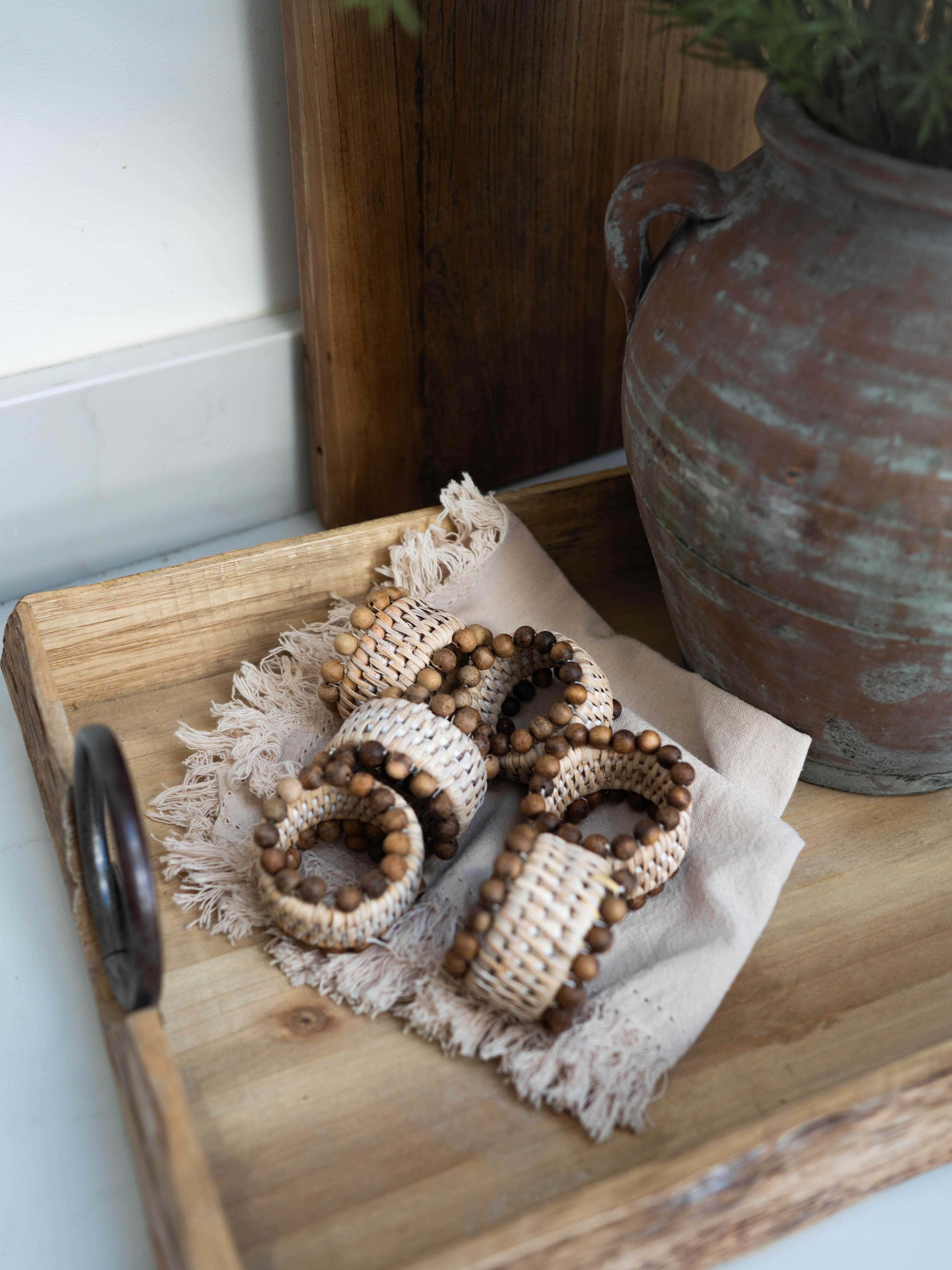 Decorative rattan napkin rings on a wooden tray with a rustic vase in the background