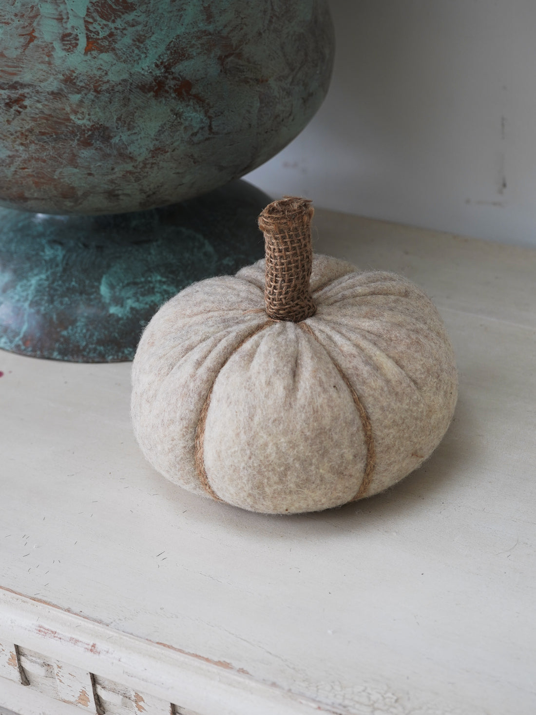 Textured beige pumpkin on a white surface with a decorative object in the background