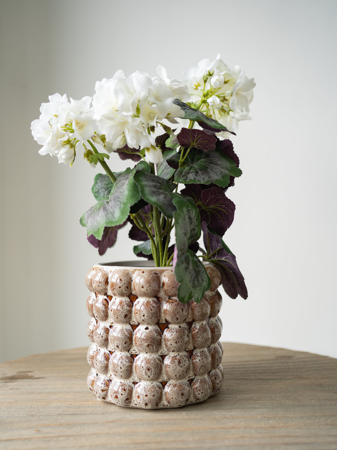 Ceramic bobble plant pot with textured surface holding white flowers on a wooden surface.