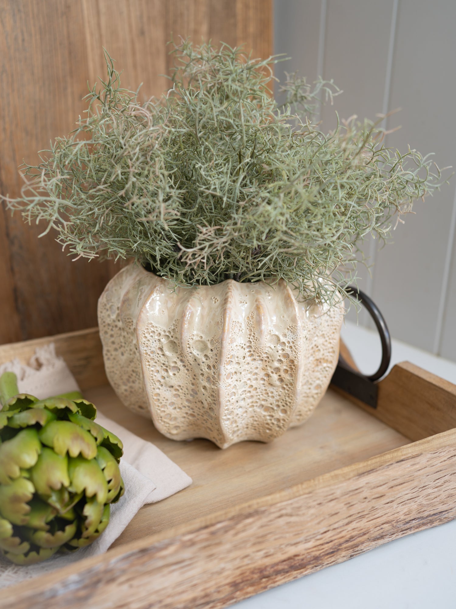 Decorative beige plant pot with greenery on a wooden tray