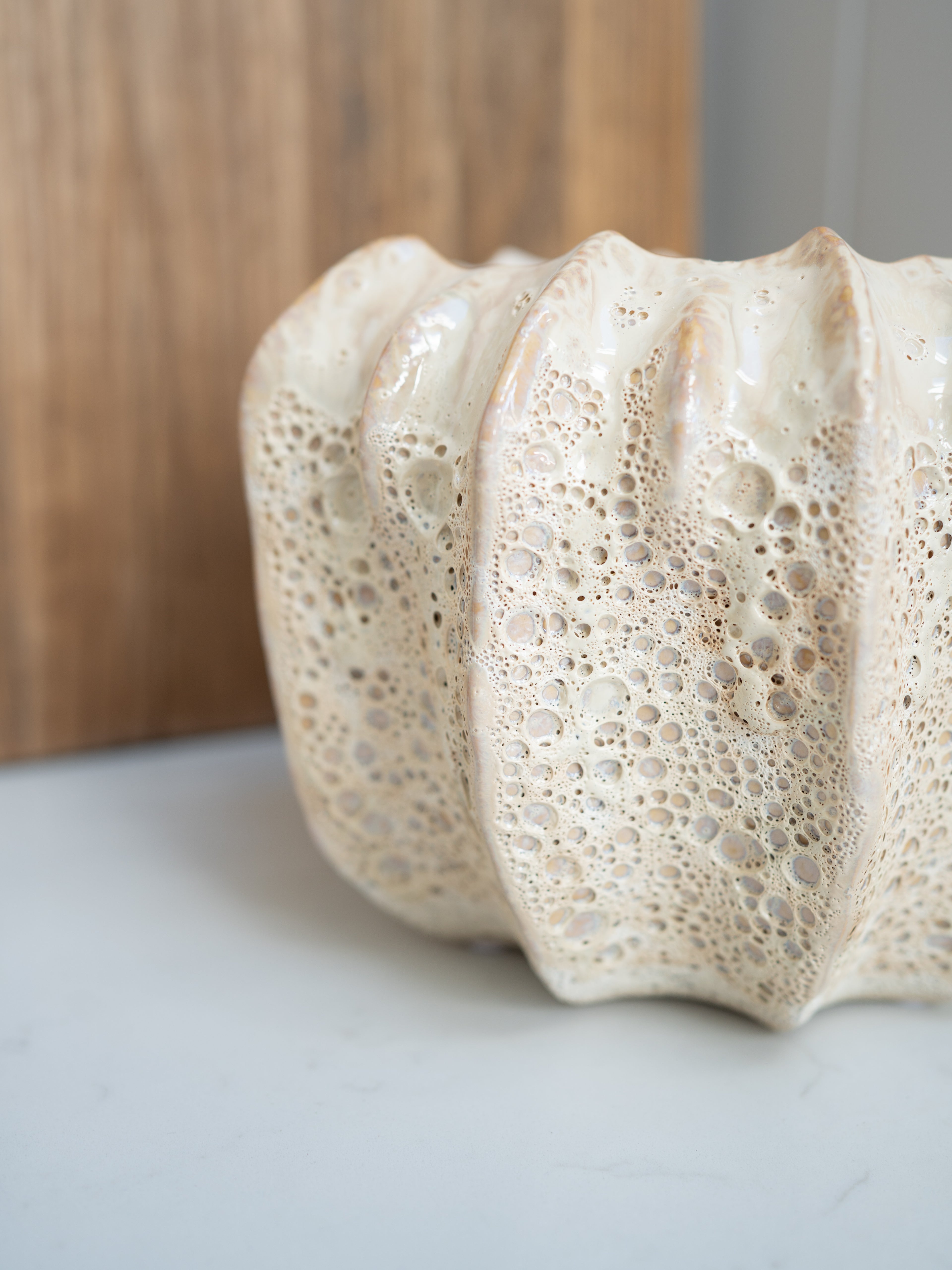 Up close of textured ceramic vase on a light surface with a wooden background
