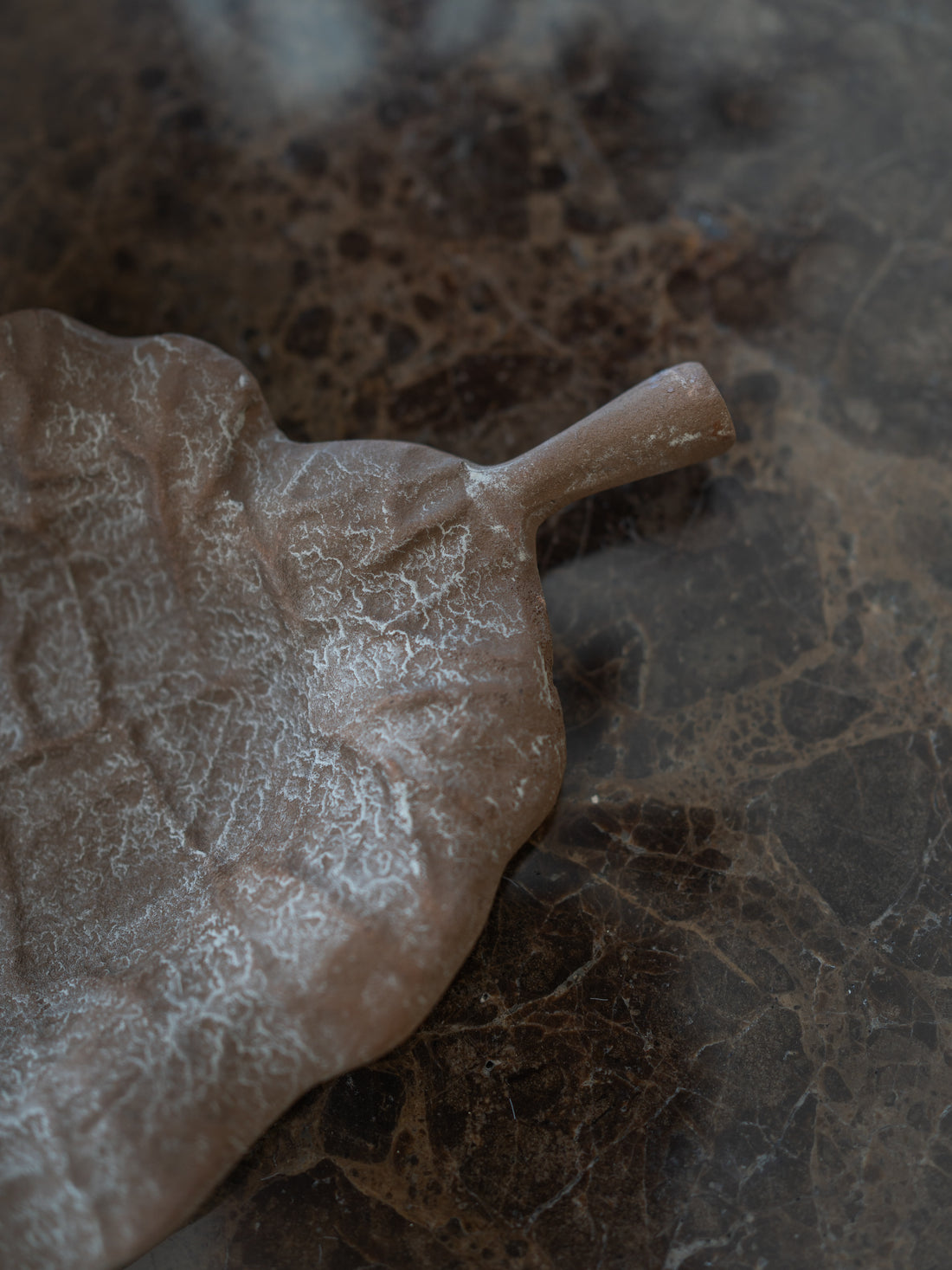 A leaf-shaped metal tray with a textured, matte finish, placed diagonally on a dark brown marble surface.