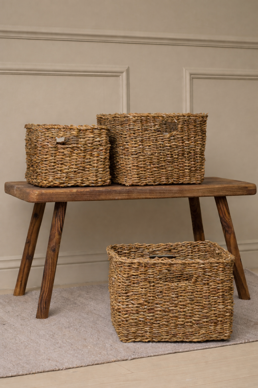 Three woven seagrass baskets on a wooden bench against a beige wall.
