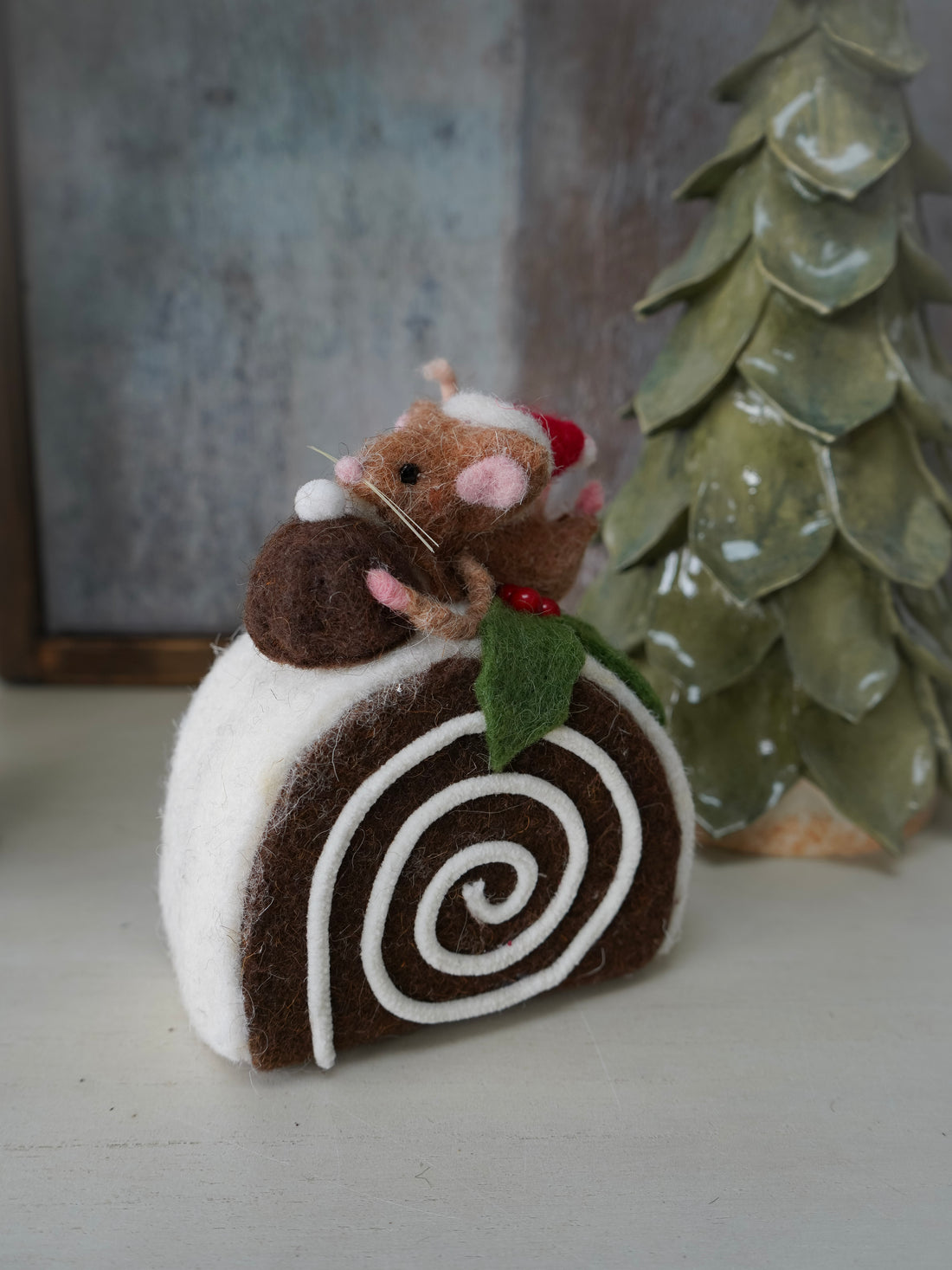 Felted mouse on a felted cake with a Christmas tree in the background