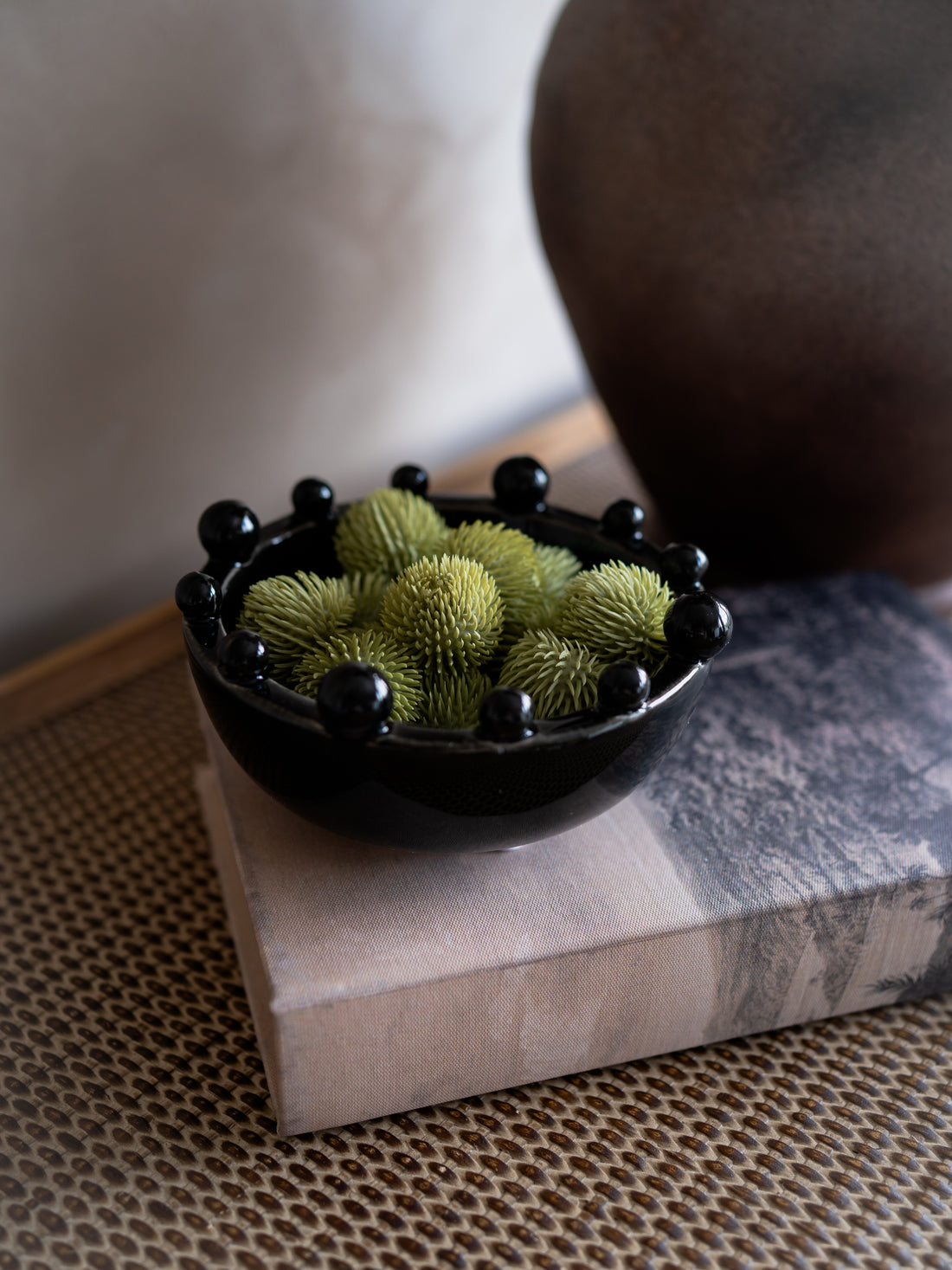 Black bowl with green spherical objects on a textured surface