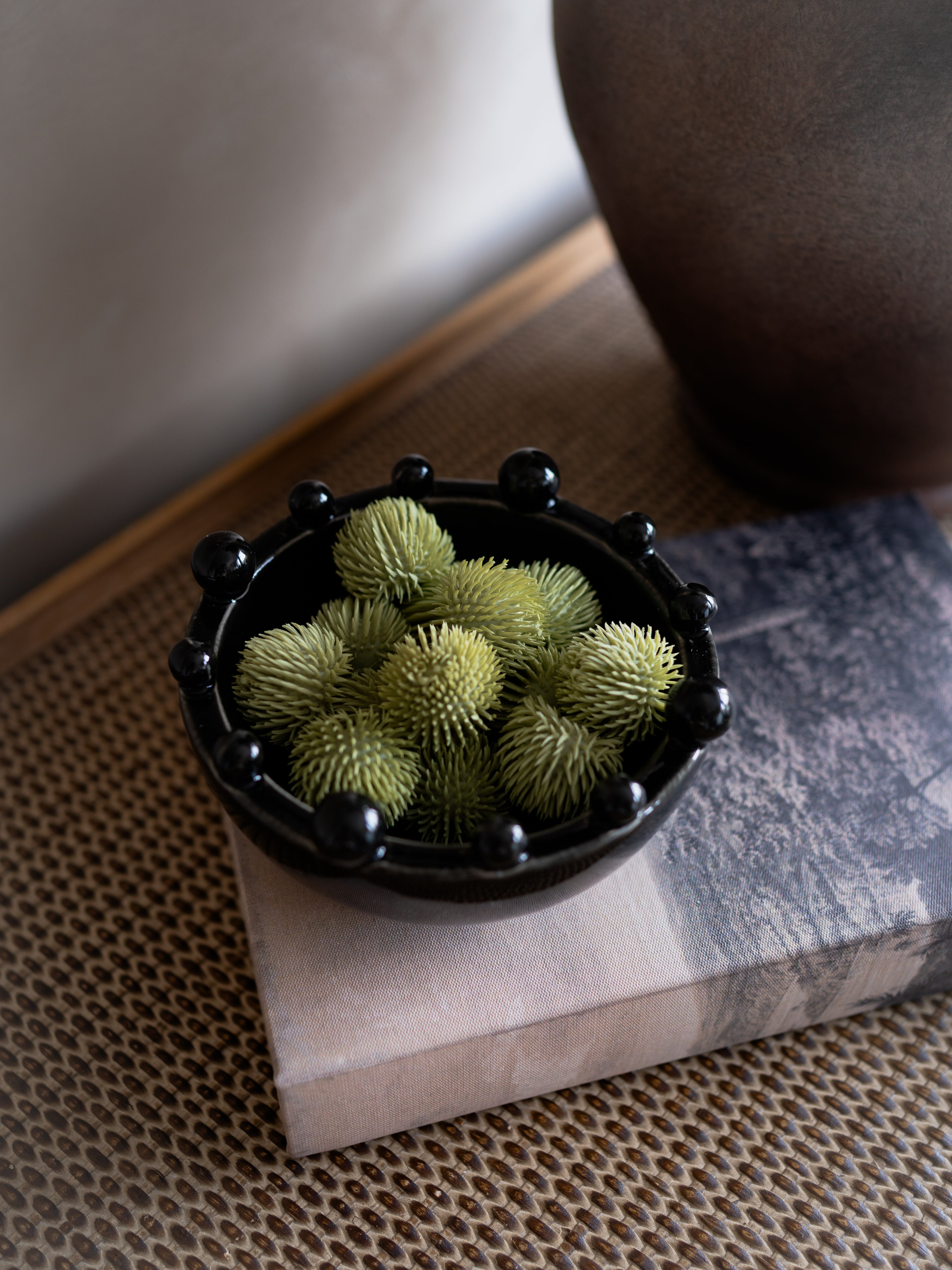 Small black bowl filled with green spherical objects on a textured surface