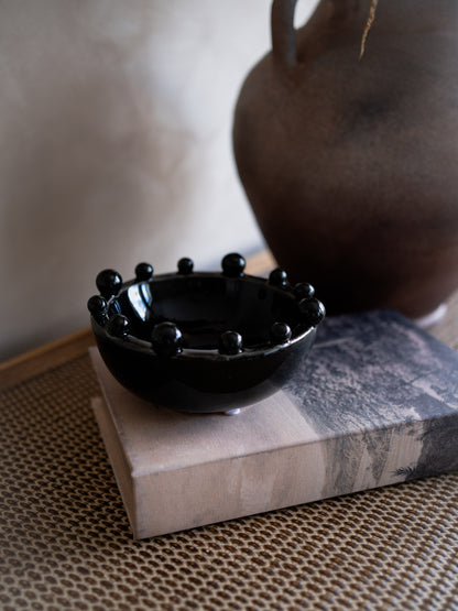 Black decorative bowl with spherical design on a textured surface