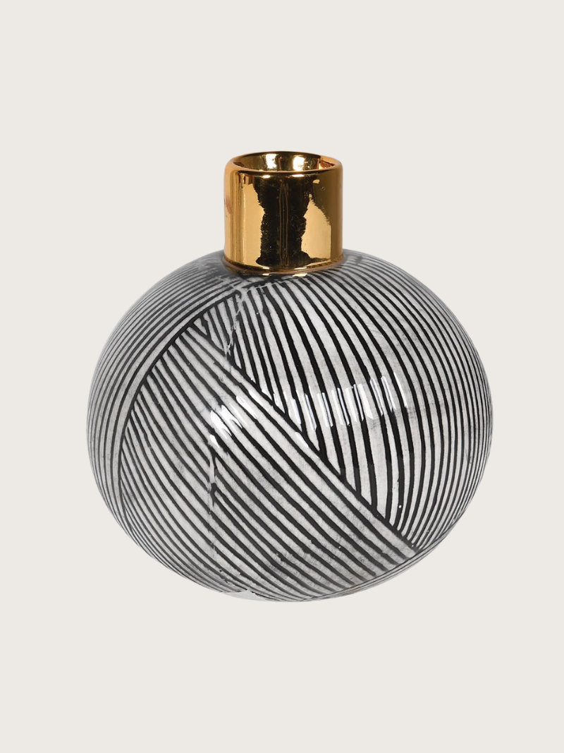 Decorative vase with black and white striped design and gold top on a light gray background