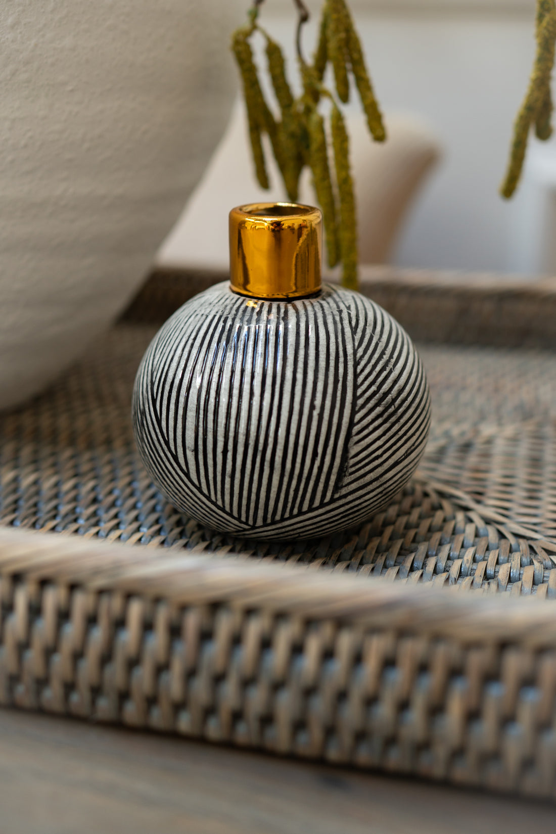 Ceramic vase with black and white pattern and gold top on woven surface