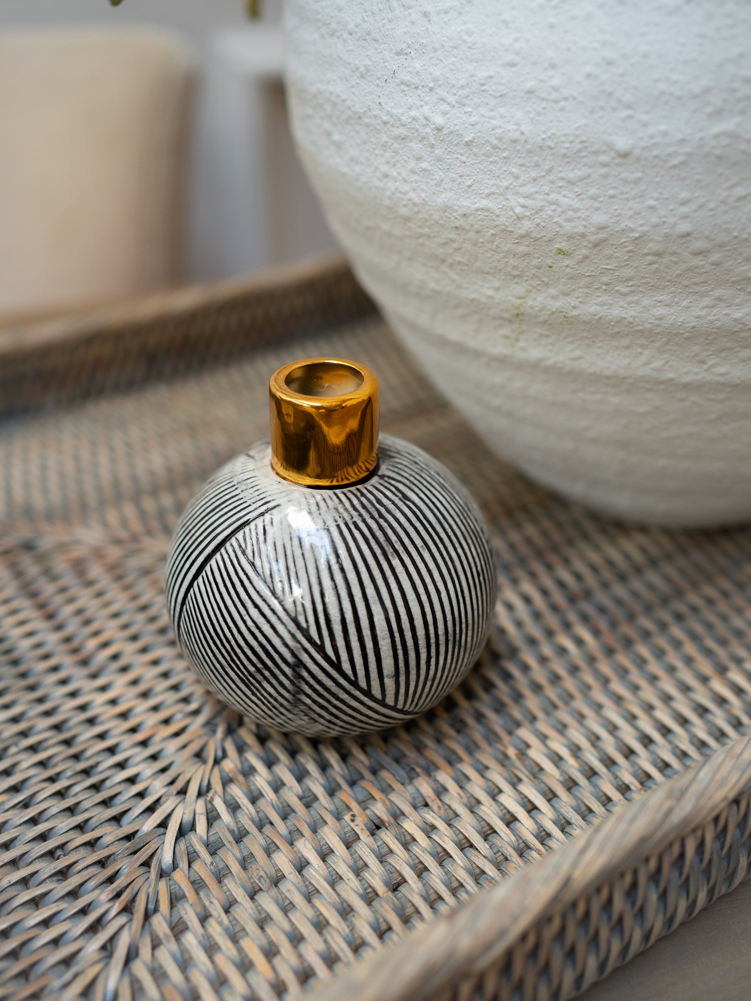 Small black and white striped vase with gold top on a textured surface