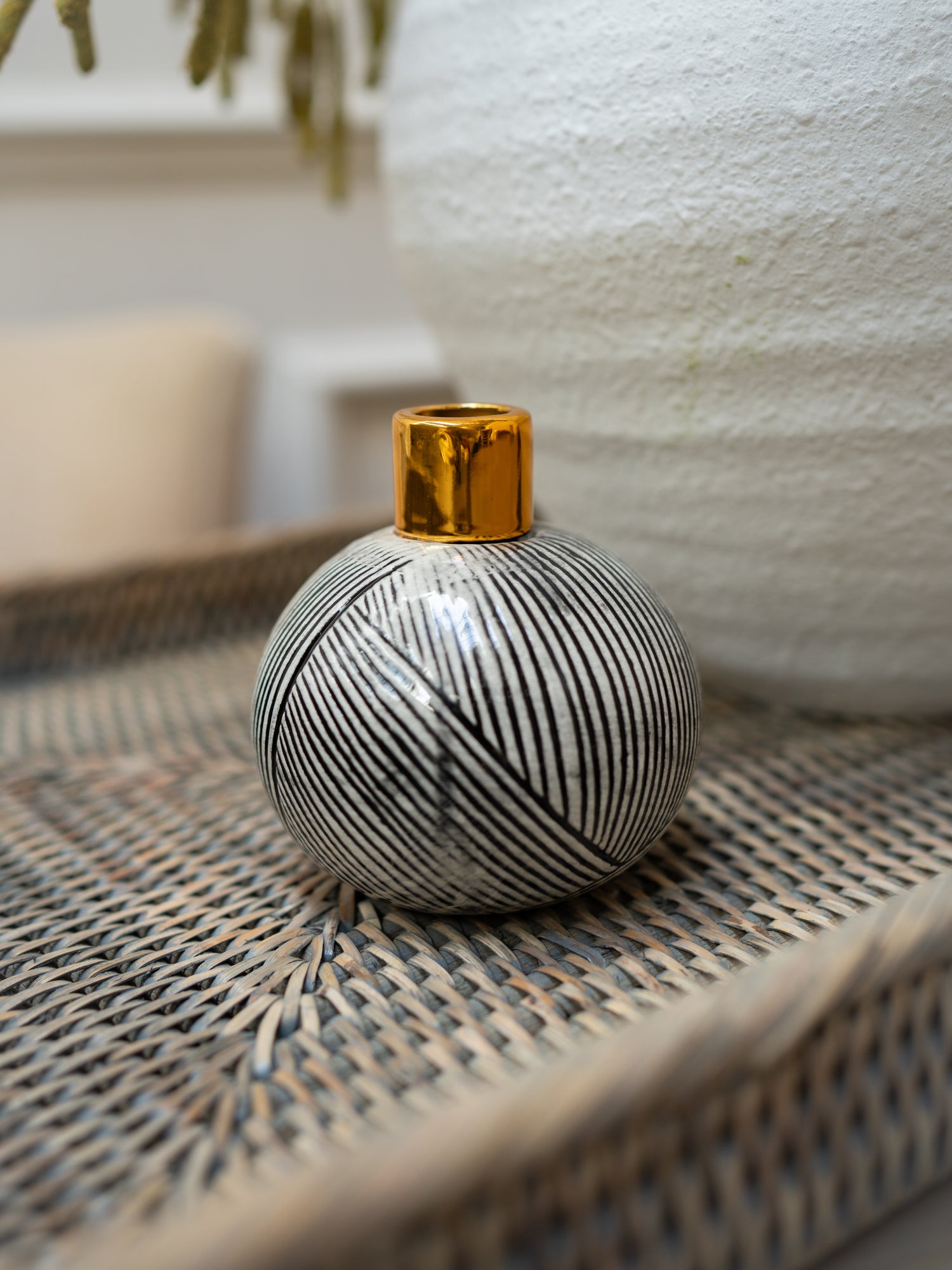 Decorative vase with black and white pattern and gold top on a woven surface