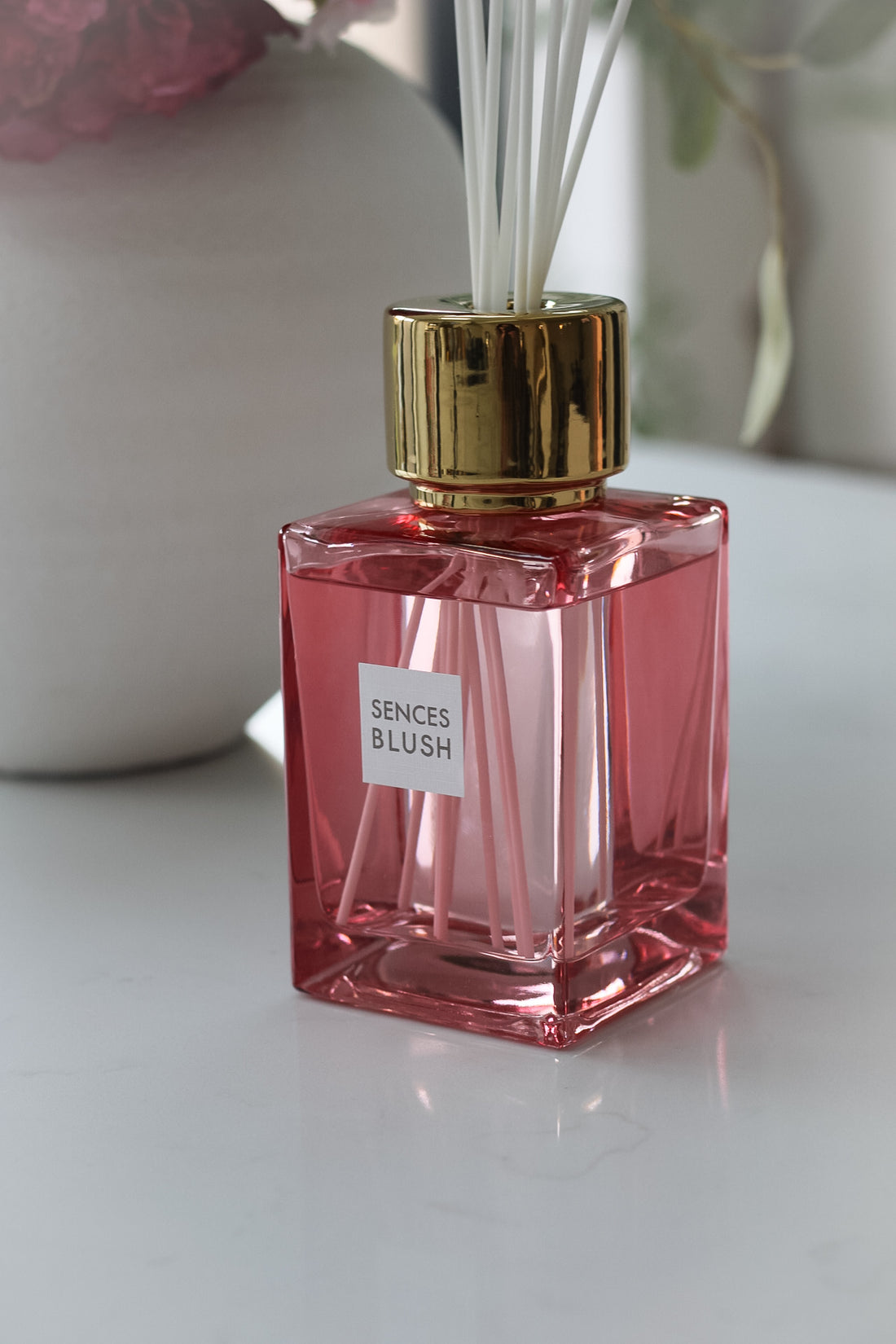 Luxury blush sences reed diffuser on white marble worktop with vase in the background