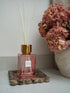 Pink diffuser with gold cap on a brown scalloped marble tray next to pink hydrangeas flowers.