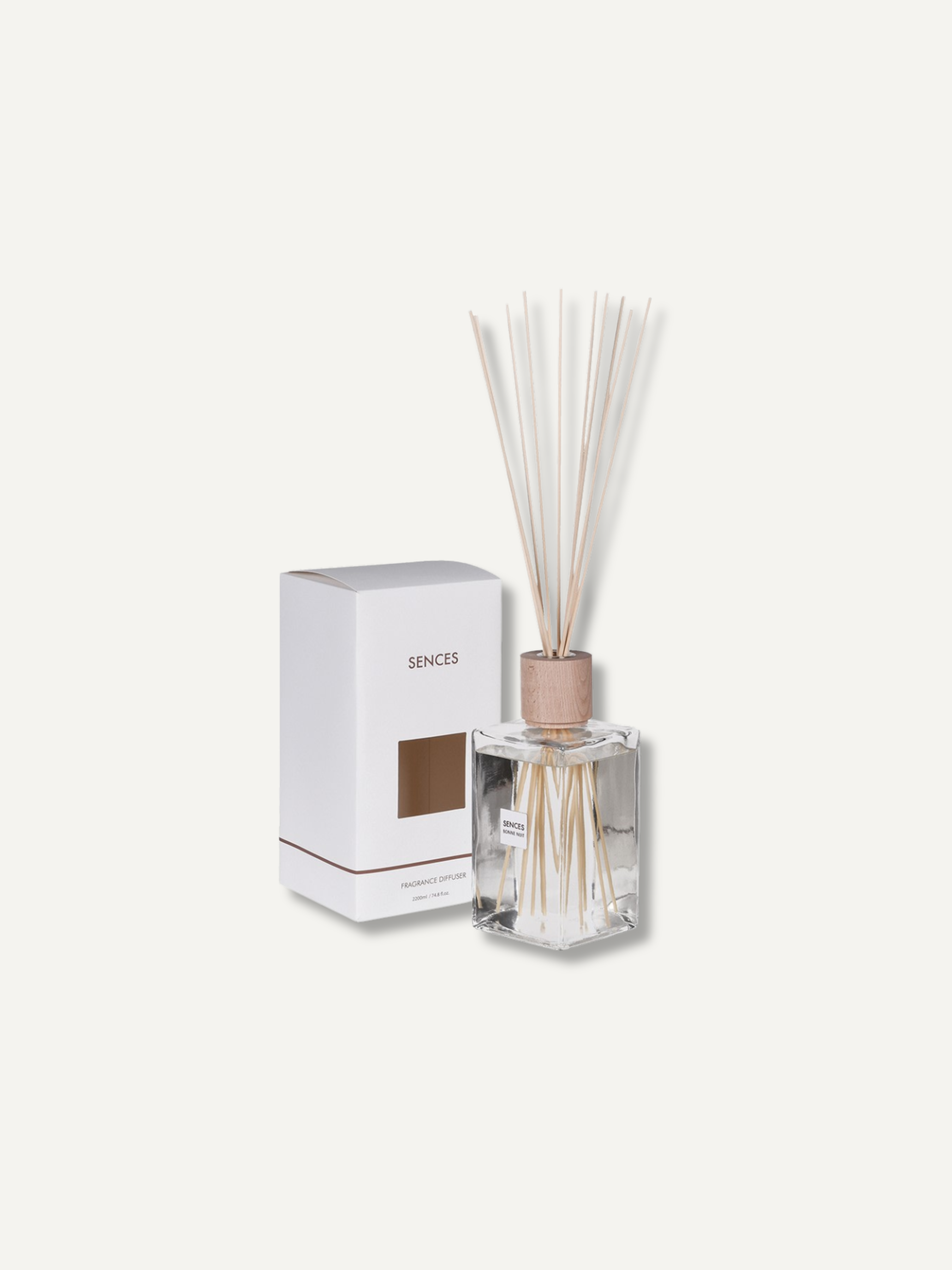 A reed diffuser bottle with light natural reeds and a metallic rose-gold cap, shown next to its white packaging box with the brand name &