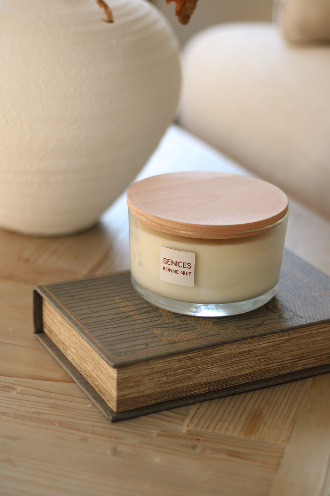 Sences candle in Bonne nuit lavender scent with wooden lid on a book, surrounded by decorative items